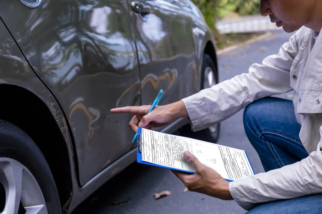 Insurance adjuster holding clipboard and examining a dent in the side of a car. If you’ve been injured in a car accident, our Kansas City car accident lawyers are ready to help you.