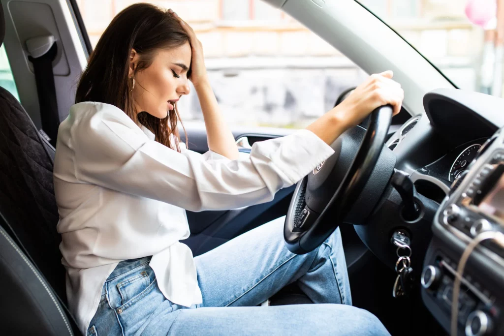 Woman driving and holding her head in pain after a car accident. If you’ve sustained an injury due to an auto accident, the motor vehicle accident attorneys at Yonke Law in Kansas City are ready to fight for the compensation you deserve.