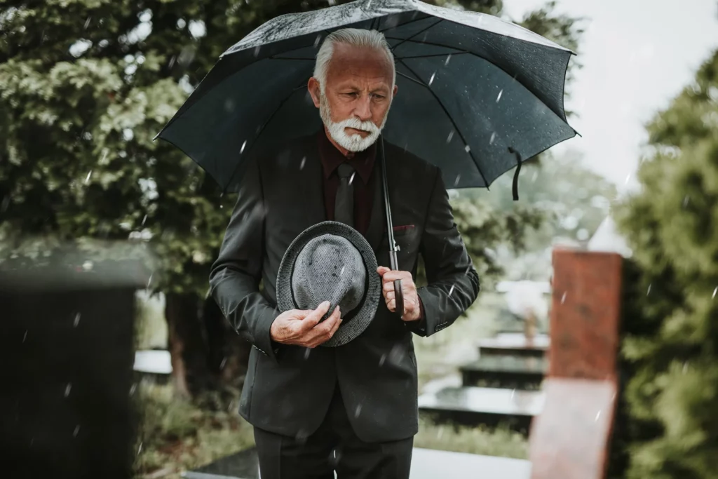 Sad elderly man visiting a tombstone in the rain. If you’ve lost a loved one due to negligence, our Kansas City wrongful death lawyers are ready to help you.
