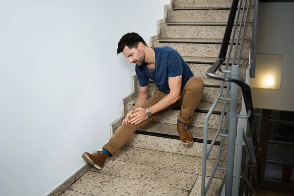 Man sitting on stairs holding his knee after slip and fall accident and needs to call a Kansas City premises liability attorney.