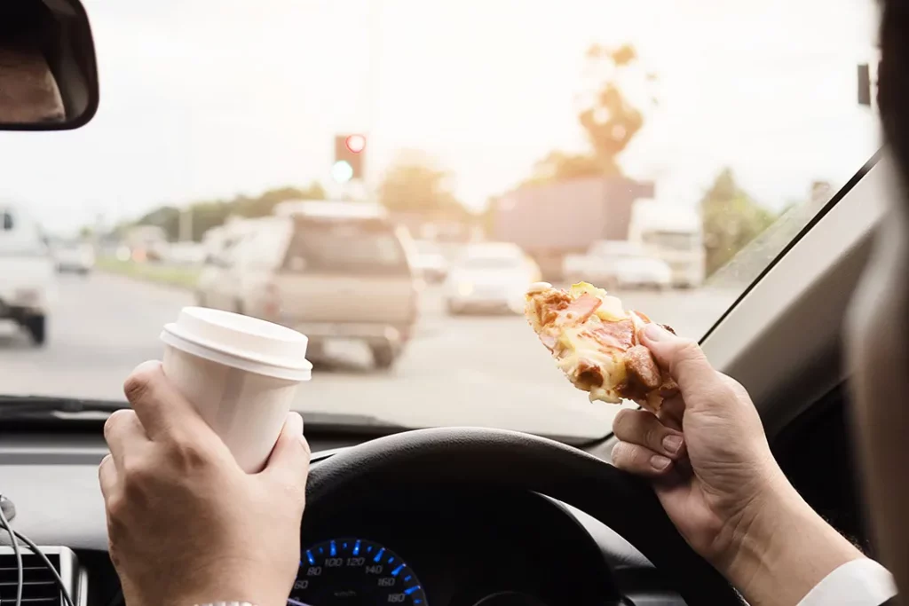 Distracted driver holding pizza and coffee cup. If you've been injured by a distracted driver, our Kansas City car accident lawyers are ready to fight for you. 