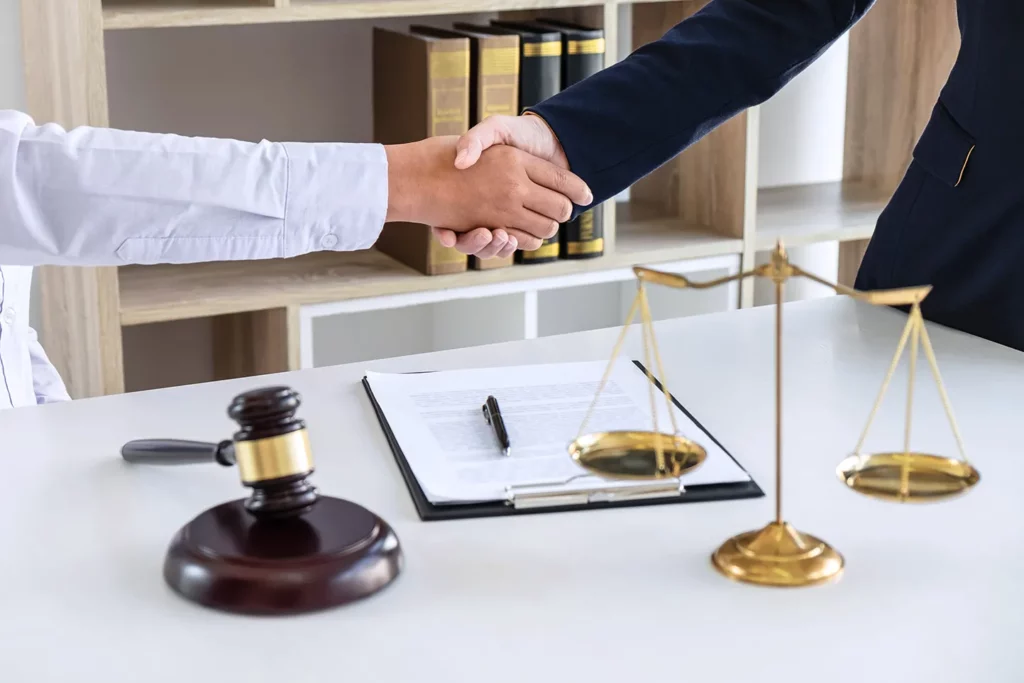 Two Kansas City personal injury lawyers shaking hands over a gavel and contract laying on a table. 