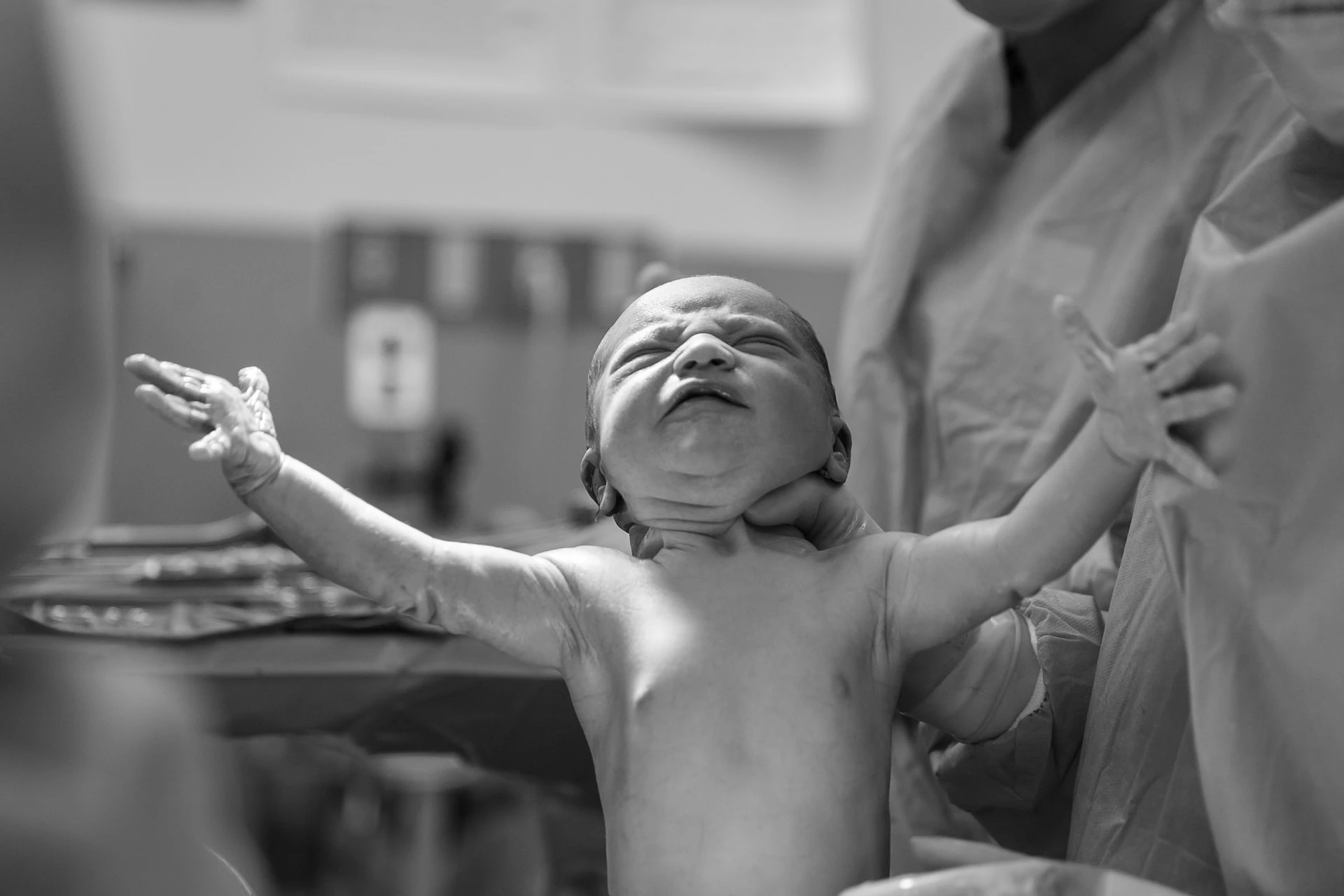 Black and white photo of a naked baby being held after birth by medical staff.